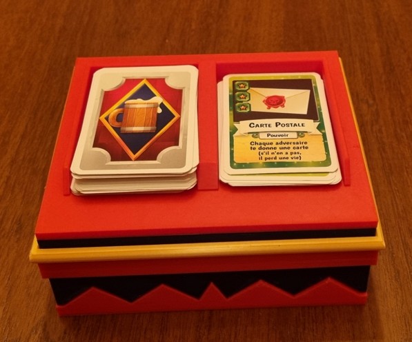 Couvercle rouge retourné servant de support de défausse pour deux piles de cartes du jeu Drinking War.